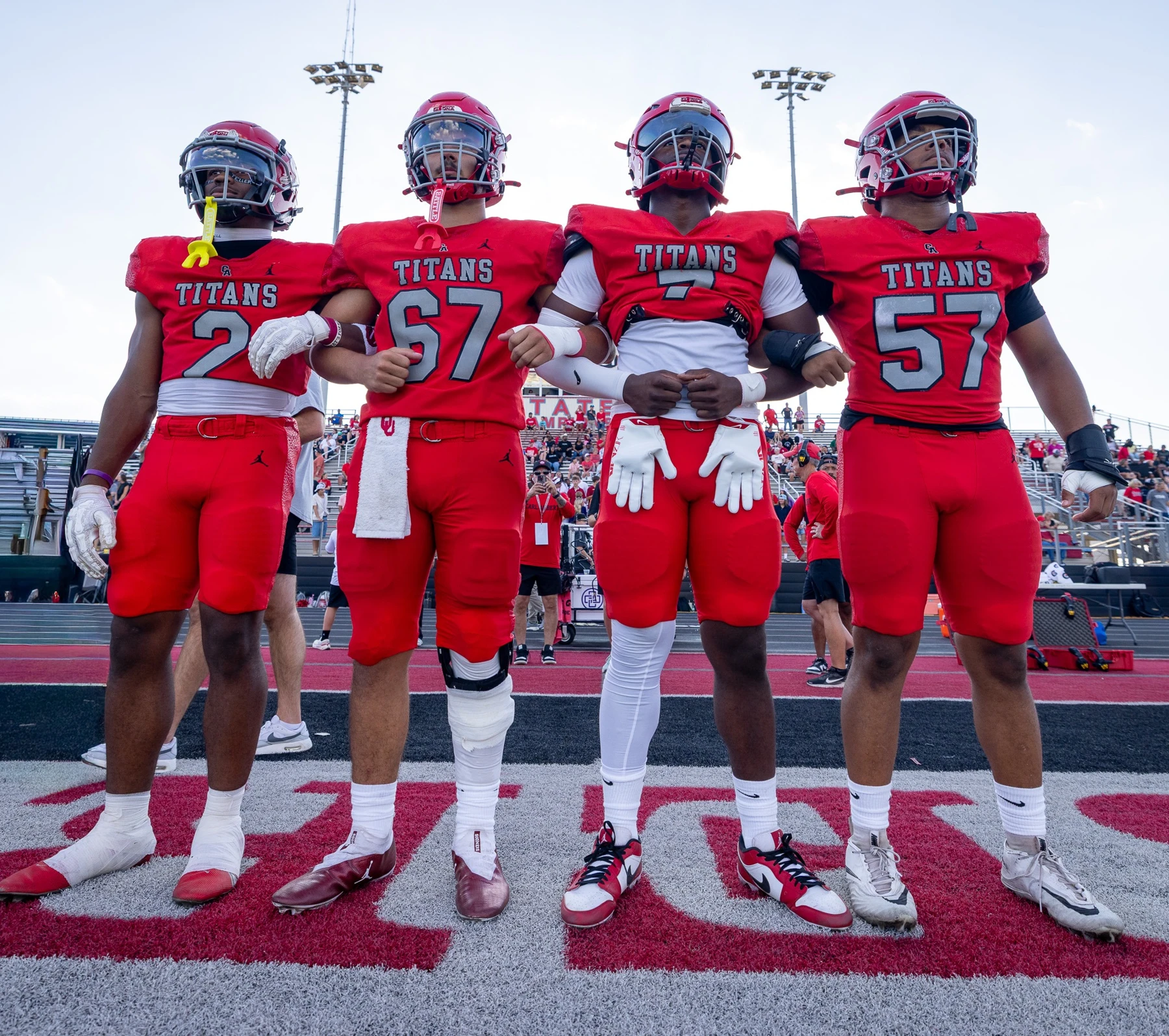 Four Carl Albert Titans football players standing arm in arm on the field